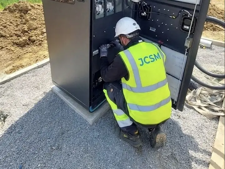 Technik JCSM kucający przed otwartą ładowarką DC na placu budowy